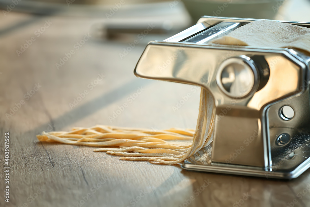 Pasta maker with dough on table in kitchen