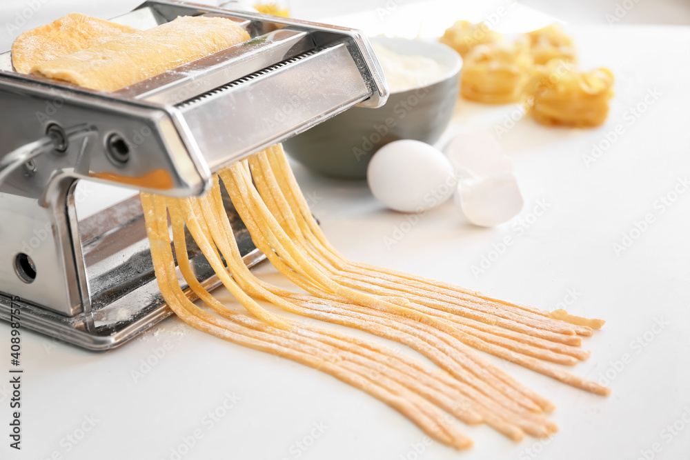 Pasta maker with dough on table in kitchen