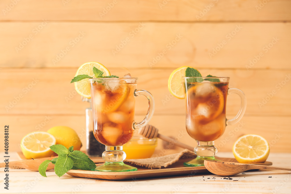 Cups of cold black tea with lemon on light wooden background