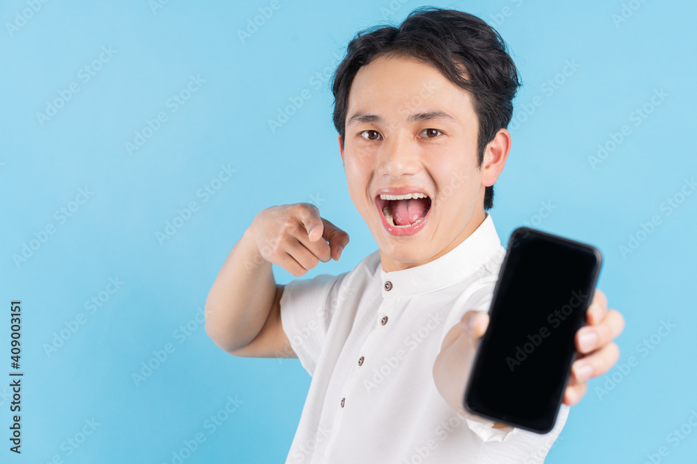 Young smiling man holding a modern smartphone in his hand and pointing his finger on blank white scr