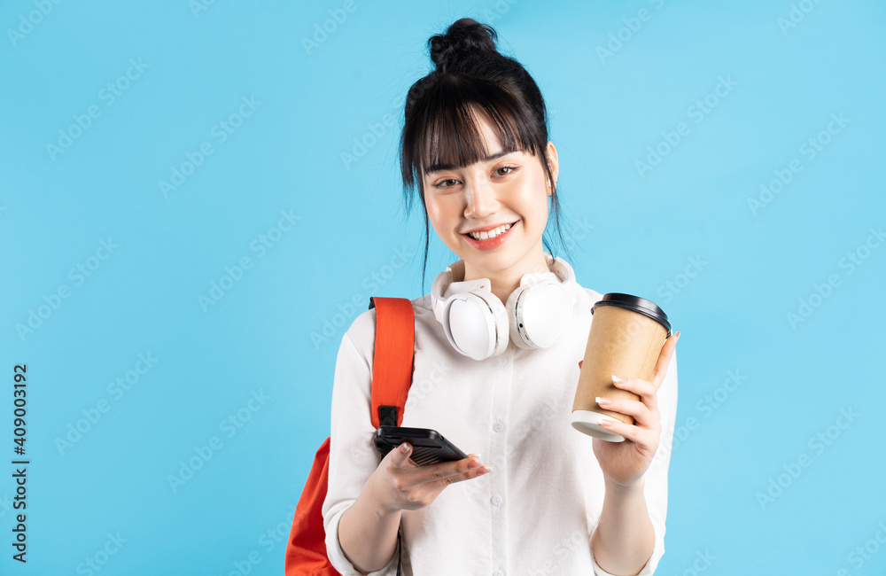 Asian female student wearing backpack behind her back, holding smartphone, neck wearing wireless ear