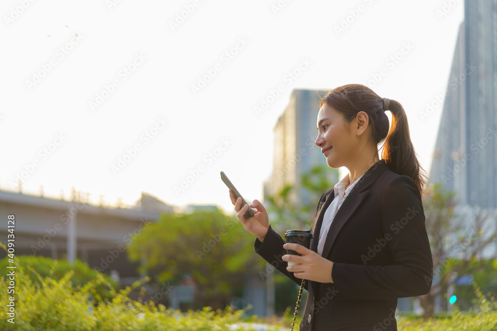 亚洲高管职场女性拿着咖啡杯在办公室的街道上使用手机