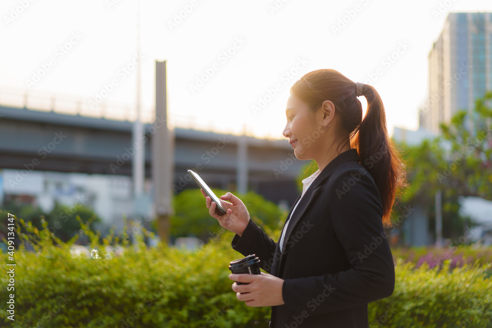 亚洲高管职场女性拿着咖啡杯在办公室的街道上使用手机