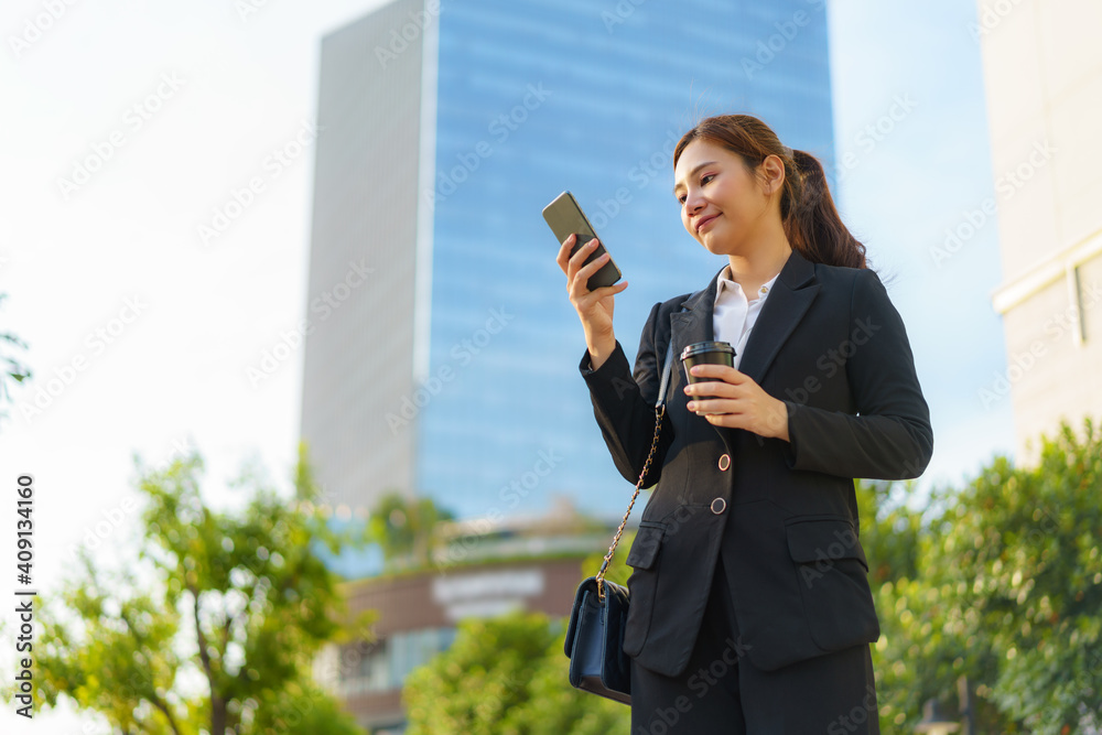 Asian executive working woman holding coffee cup and using a mobile phone in the street with office 