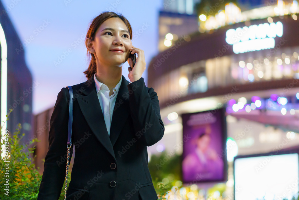 亚洲高管职场女性在后面有办公楼的街道上使用手机