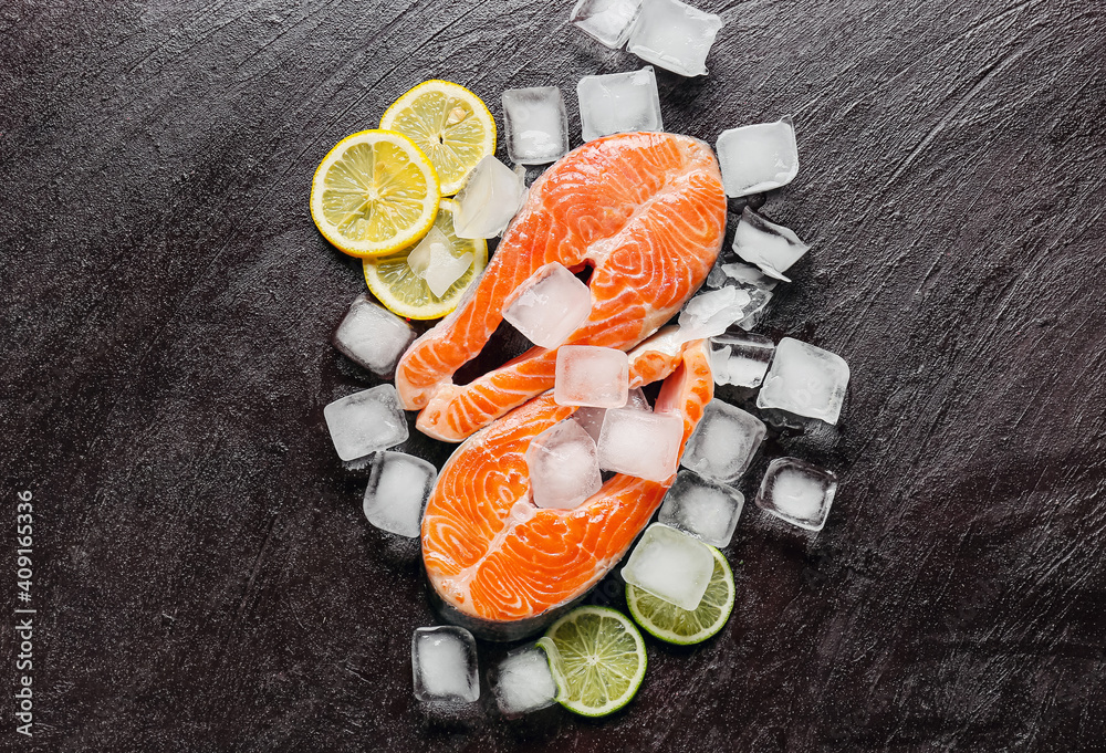 Raw salmon steaks, ice cubes and lemon on dark background