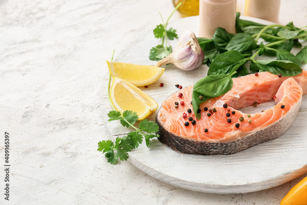 Plate with raw salmon steak, herbs and spices on light background