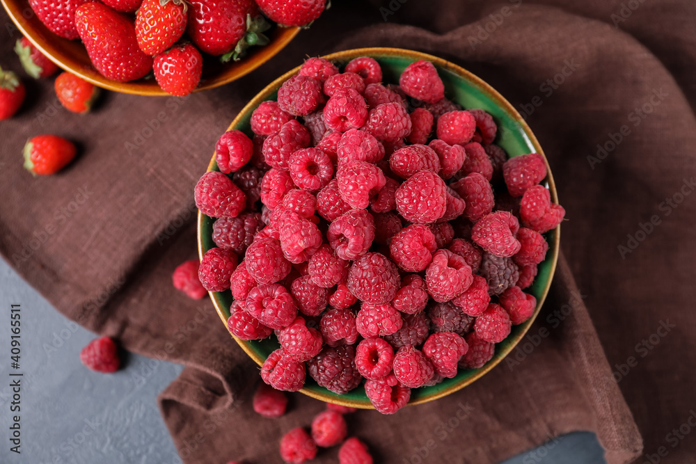 Bowls with ripe strawberry and raspberry on dark background