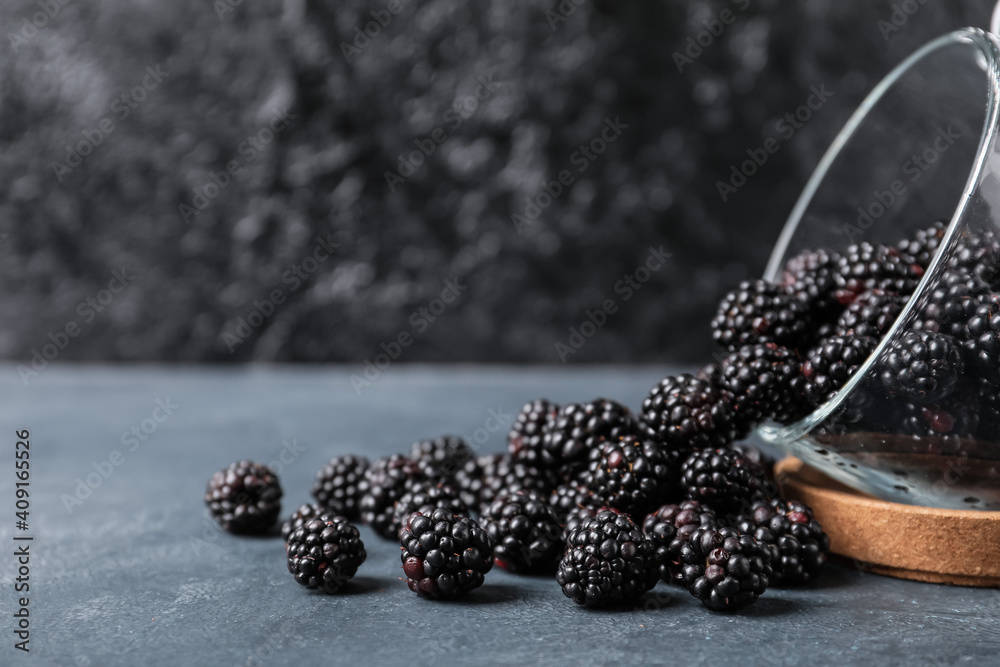 Overturned cup with ripe blackberry on dark background