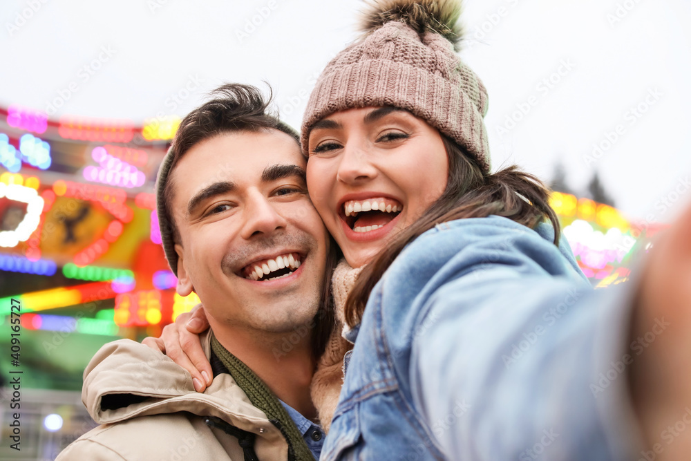 Happy young couple taking selfie in amusement park on Christmas eve