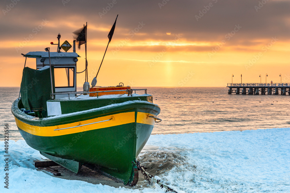 日出时，波兰波罗的海Gdynia Orlowo雪地海滩上的渔船。