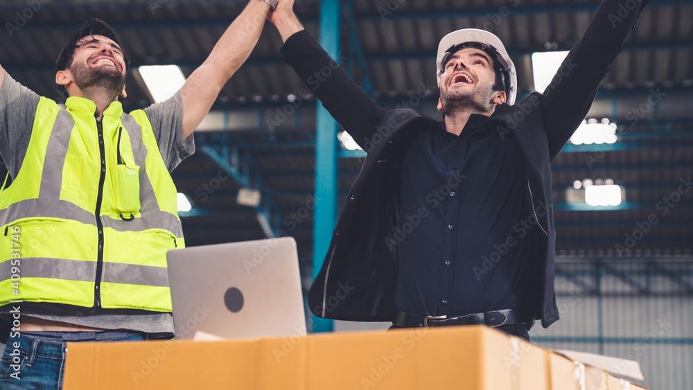 Two factory worker celebrate success together in the factory or warehouse . Industry work achievemen