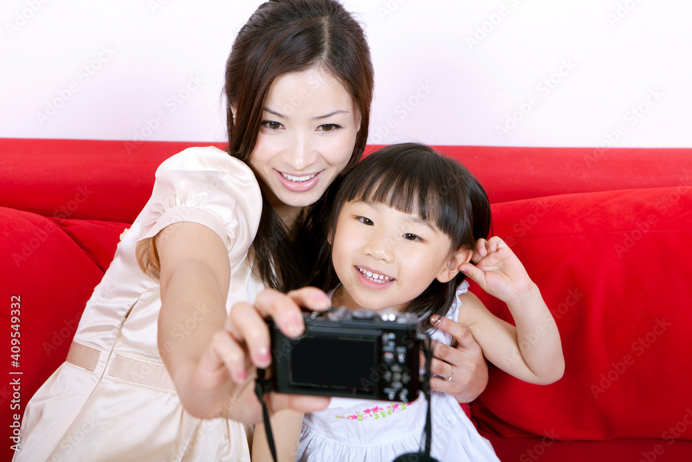 Mother with daughter photographing themselves with digital camera, smiling