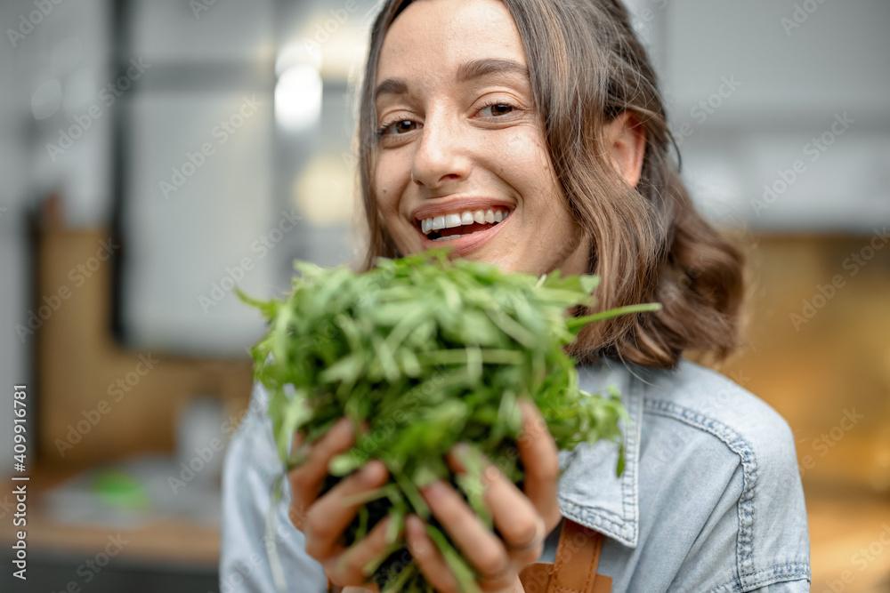 美丽微笑的女人穿着围裙，厨房里放着新鲜的芝麻菜。健康烹饪理念