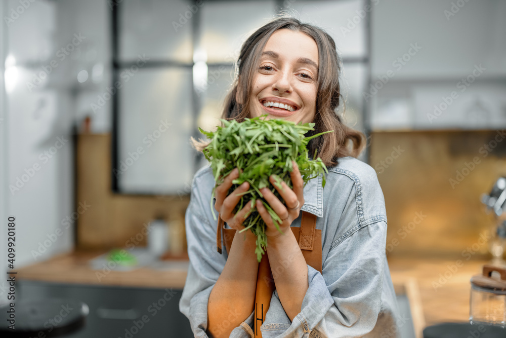 美丽微笑的女人穿着围裙，厨房里放着新鲜的芝麻菜。健康烹饪理念