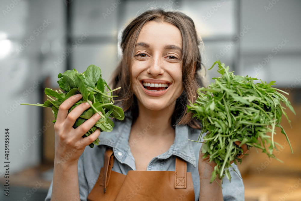 穿着围裙的快乐女人的画像，厨房里放着新鲜的菠菜和芝麻菜。健康烹饪c