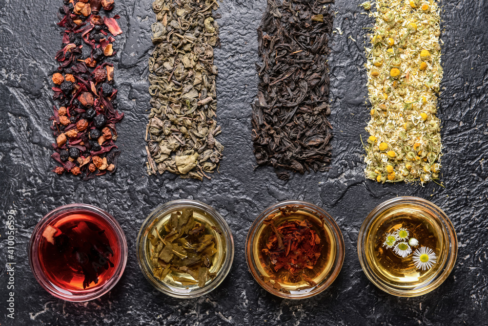 Composition with cups and different dry tea leaves on dark background