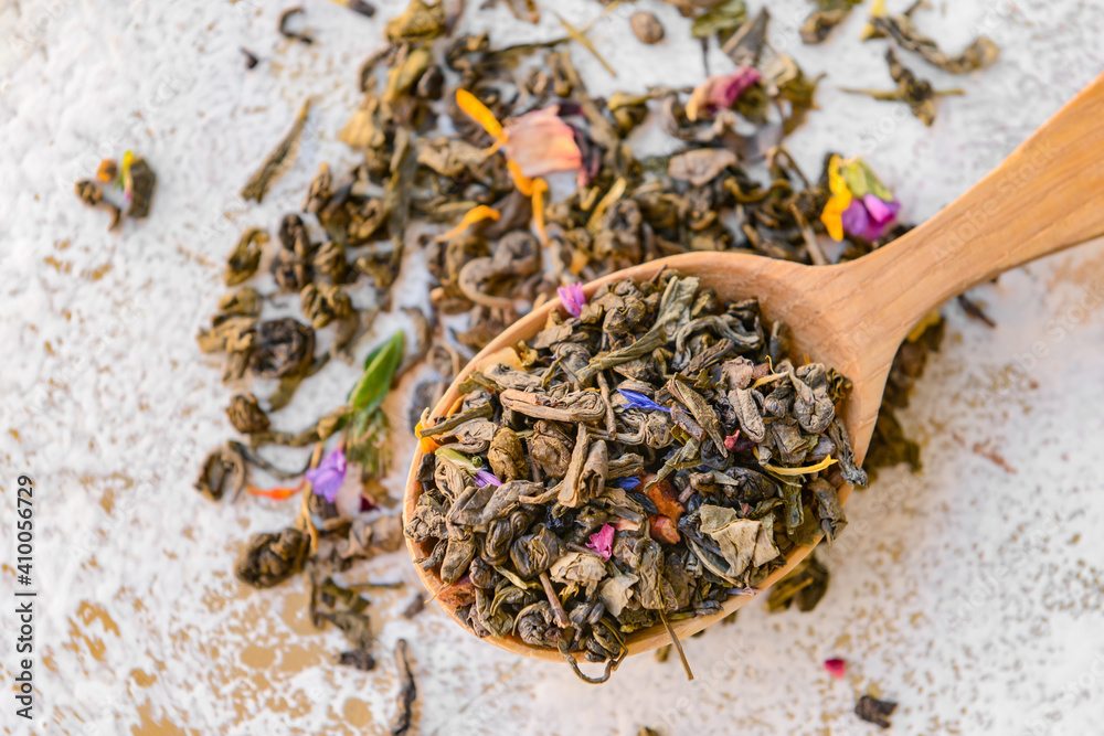 Wooden spoon with dry tea leaves and flowers on light background