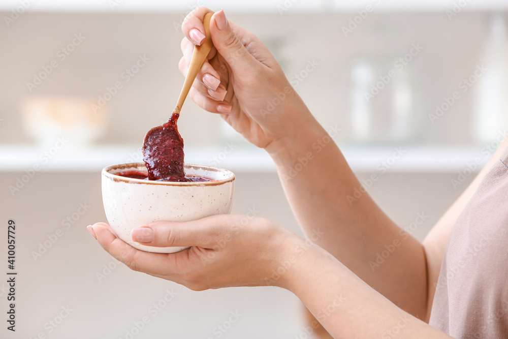 Woman with bowl of delicious homemade plum jam at home