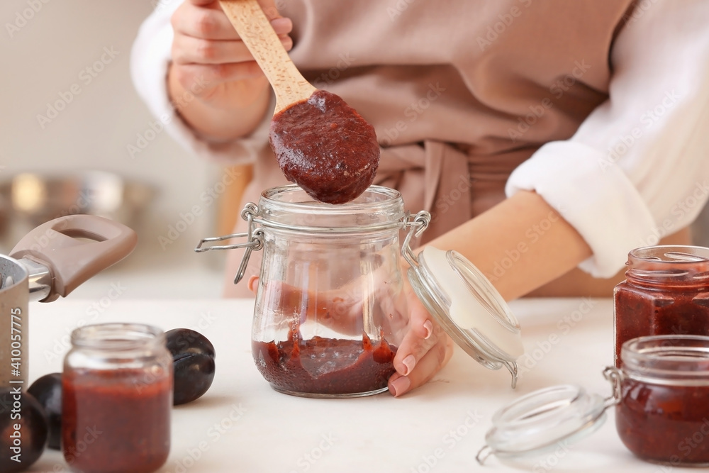 Woman pouring delicious homemade plum jam into jar