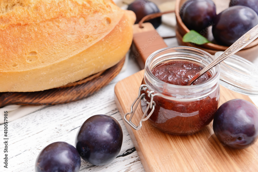 Glass jar with delicious homemade plum jam on wooden background