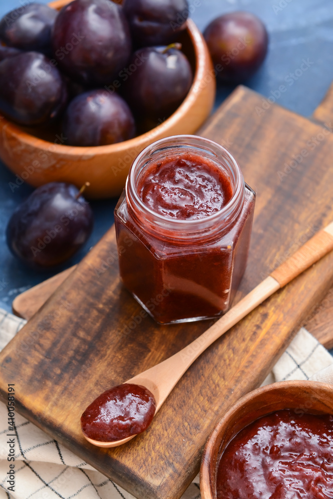 Glass jar with delicious homemade plum jam on wooden board