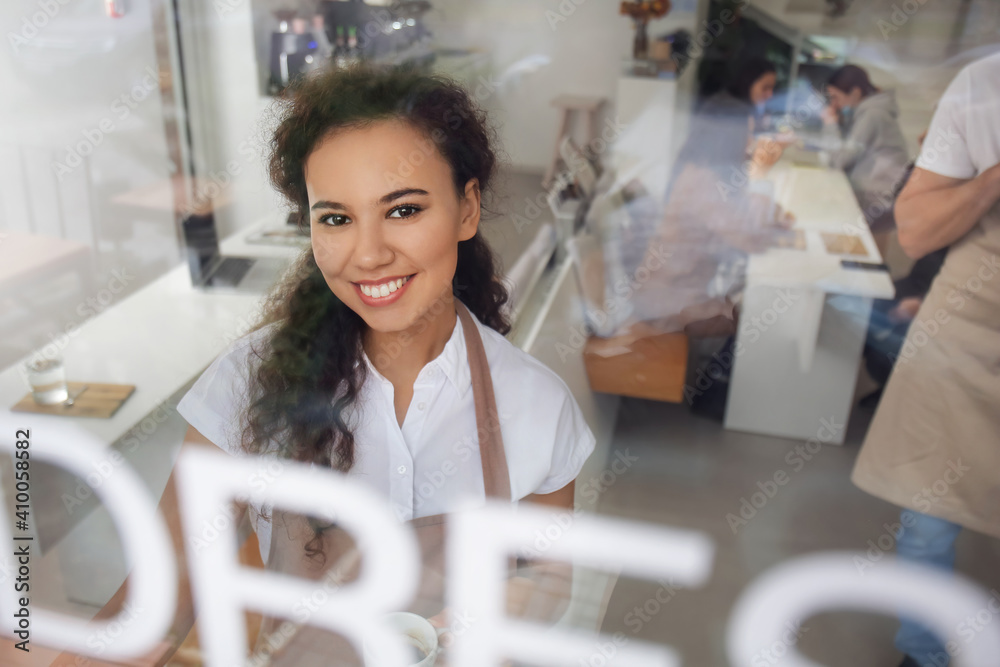 Young barista in cafe, view through glass door