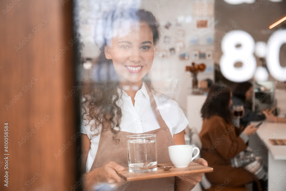 Young barista with cup of hot espresso in cafe, view through glass door