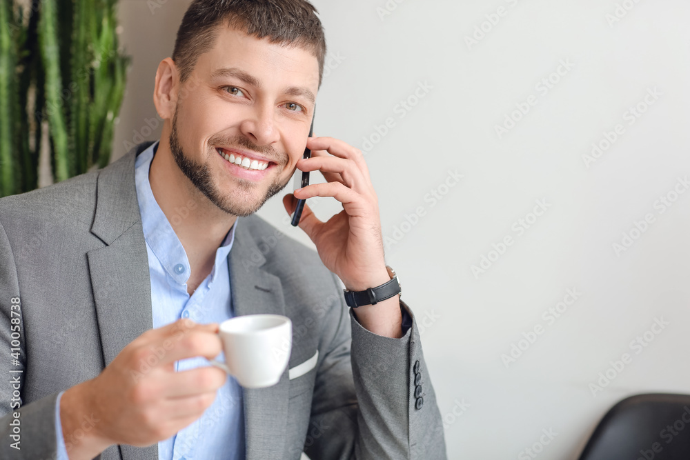 Handsome man with mobile phone and cup of hot espresso in cafe