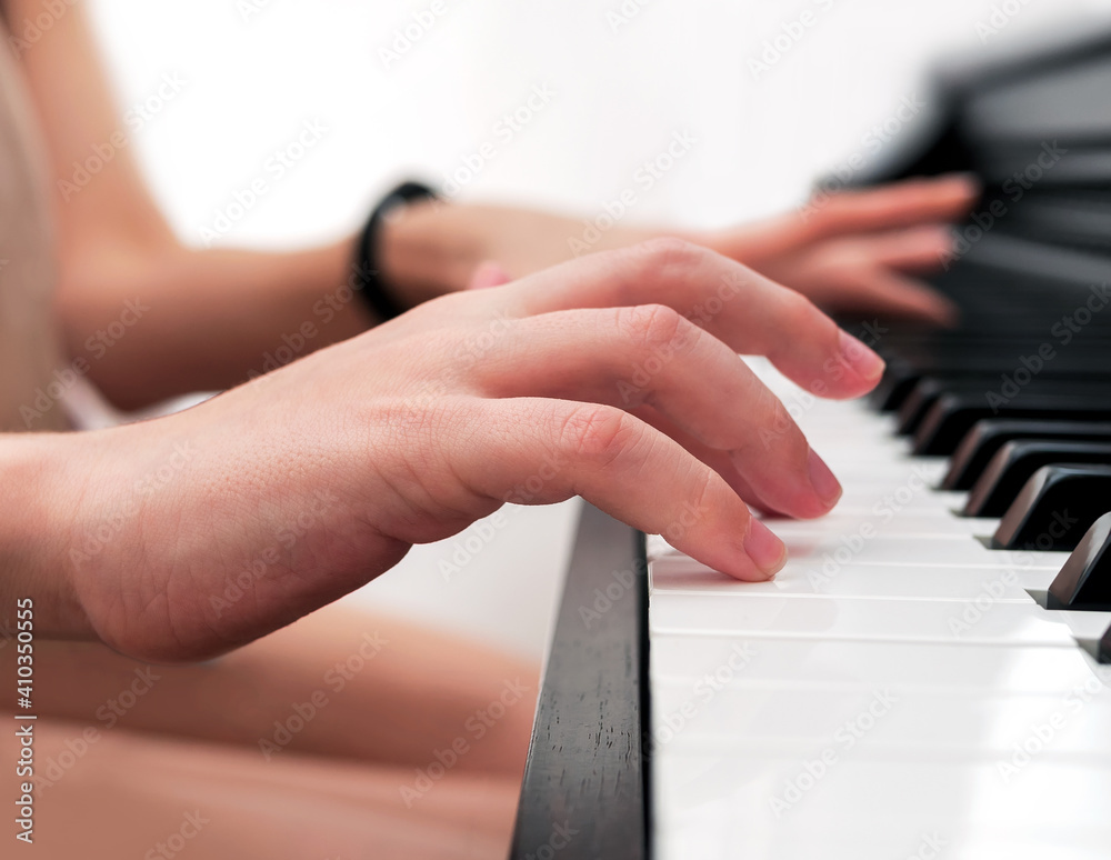 Young woman teaches a kid to play the piano. Playing together. No faces. Close-up