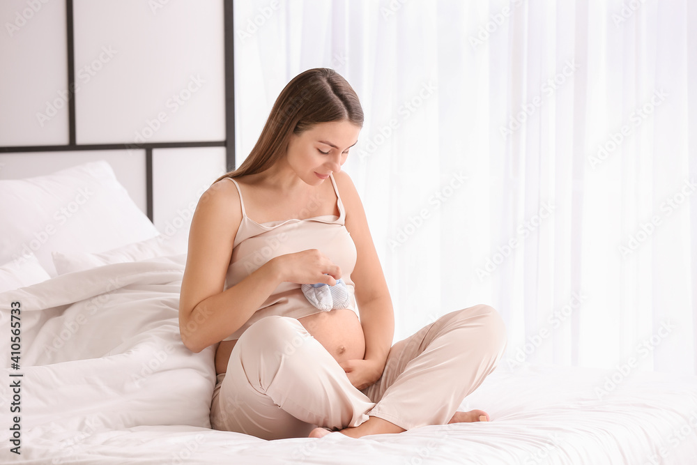 Beautiful pregnant woman with baby shoes at home