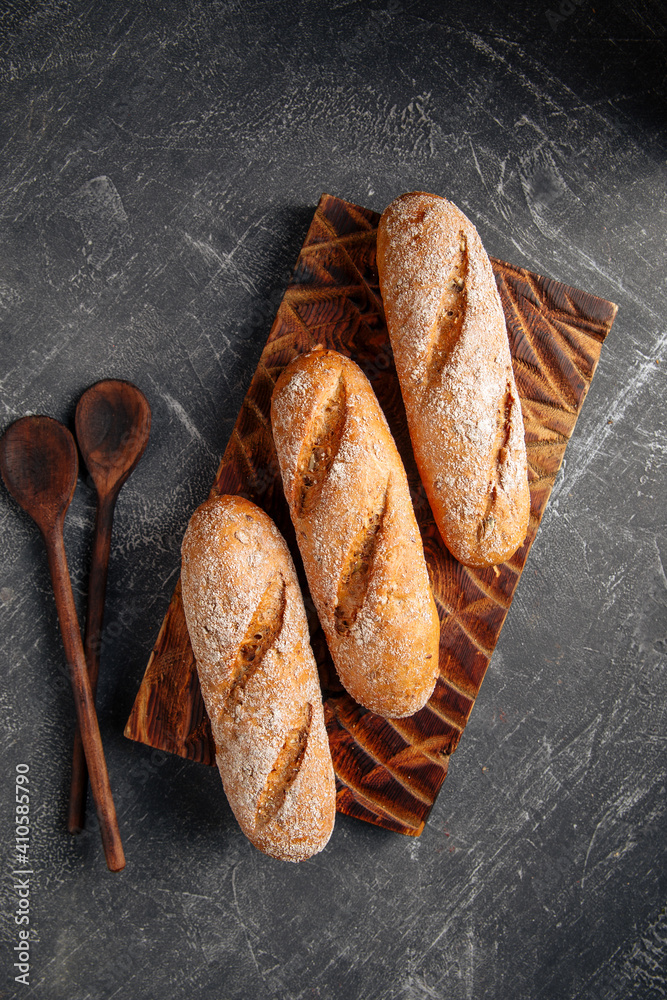 Three loafs of fresh baked baguette on the wooden cutting board on gray background