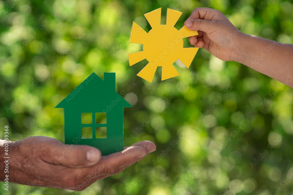 Family holding eco house in hands against spring green background