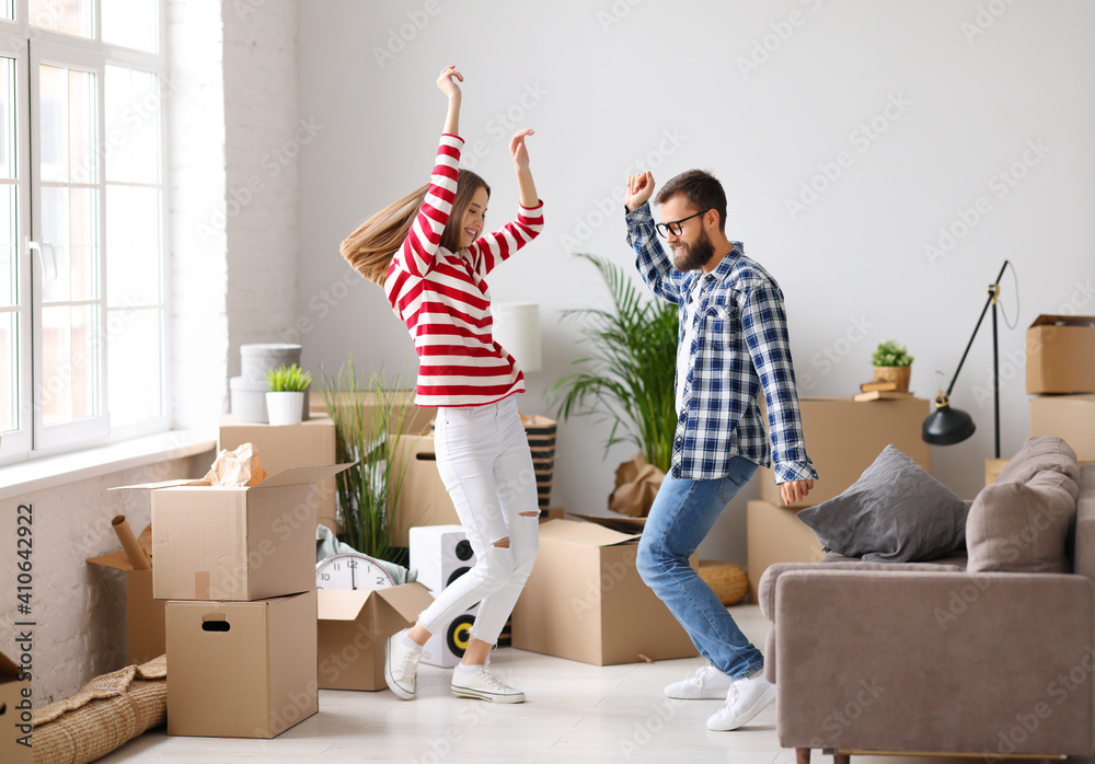 Cheerful couple dancing in new apartment with packed boxes