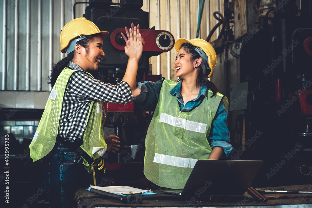 Two factory job worker celebrate success together in the manufacturing workshop or warehouse . Indus