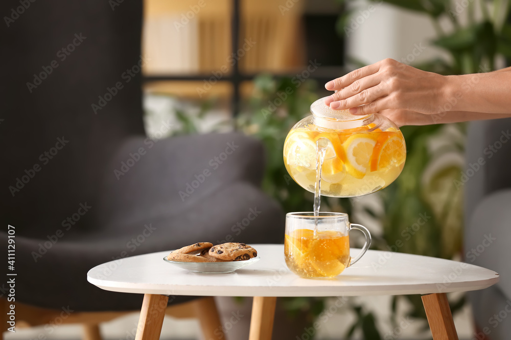 Woman pouring hot tea from teapot into cup at table