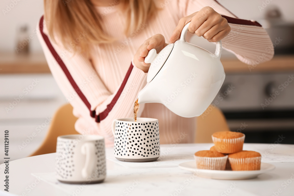 女人把热茶从茶壶倒进桌上的杯子