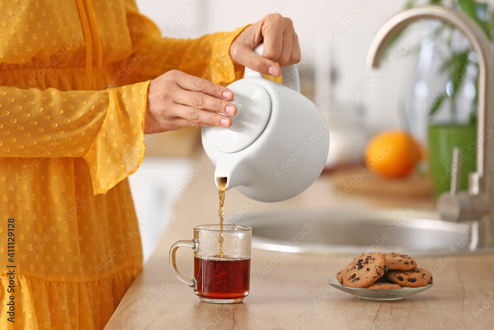 女人在厨房里把茶壶里的热茶倒进杯子里