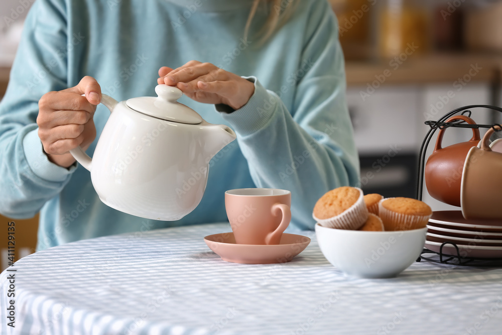 女人把茶壶里的热茶倒进桌子上的杯子里