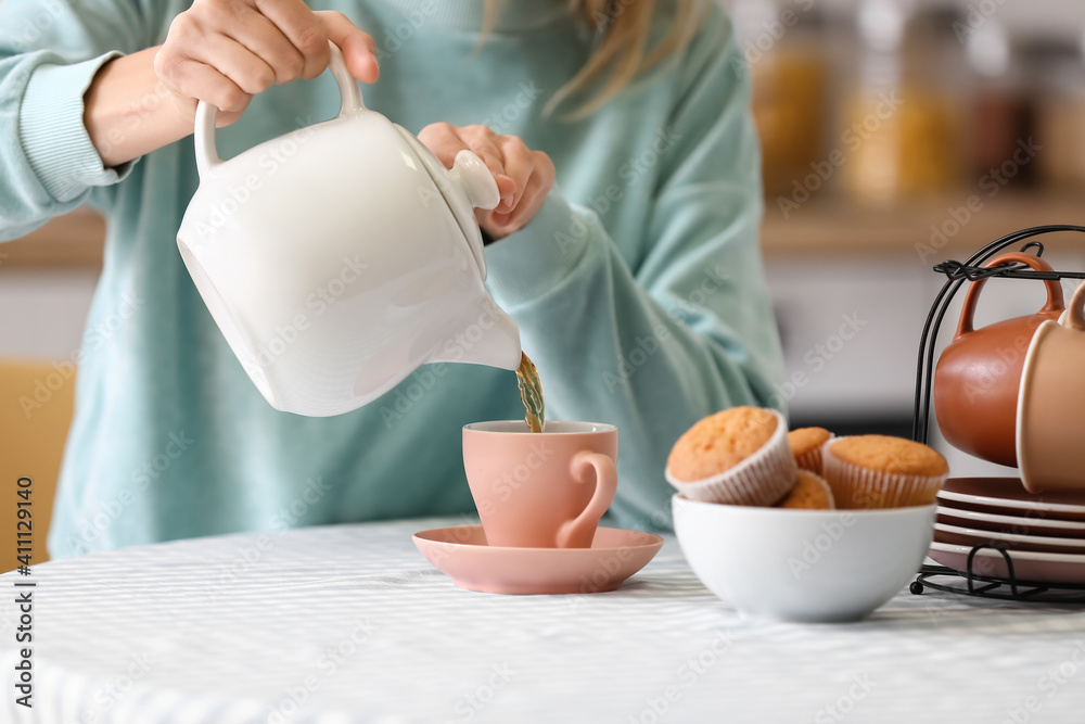 女人把茶壶里的热茶倒进桌子上的杯子里