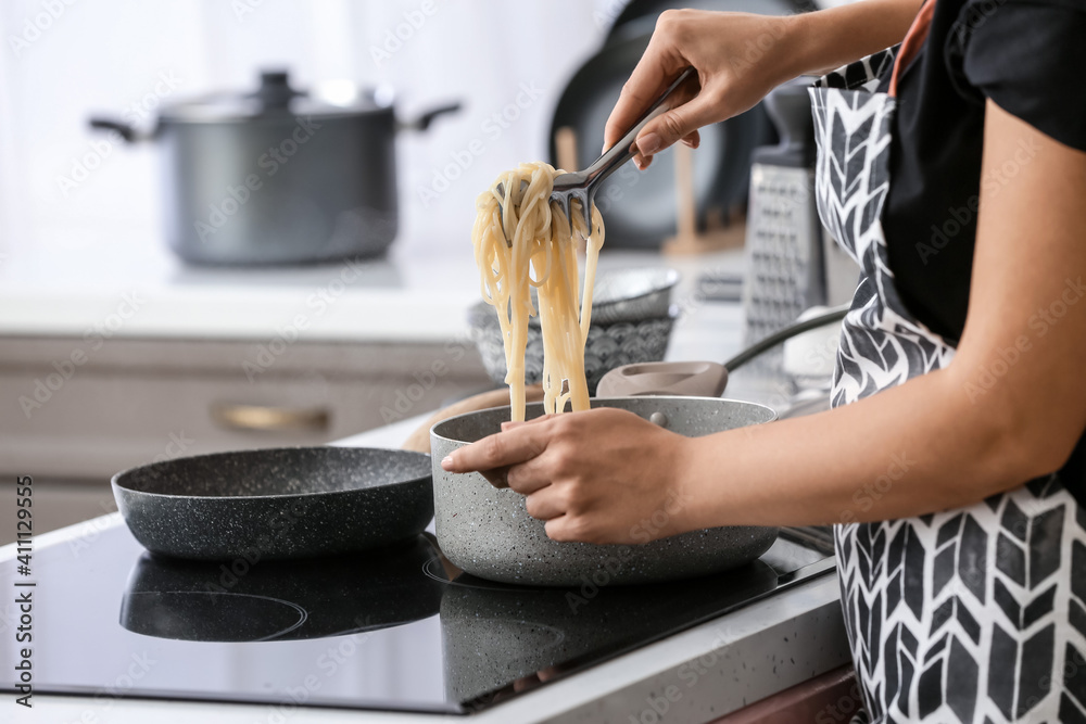 Woman cooking tasty pasta in kitchen