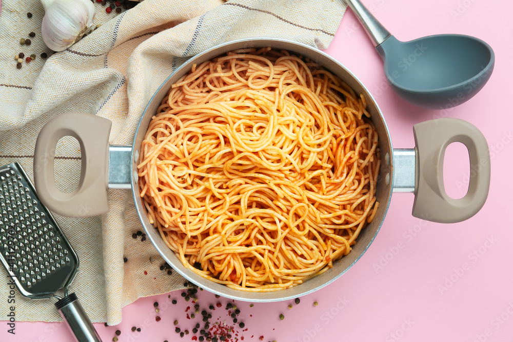 Cooking pot with pasta and utensils on color background