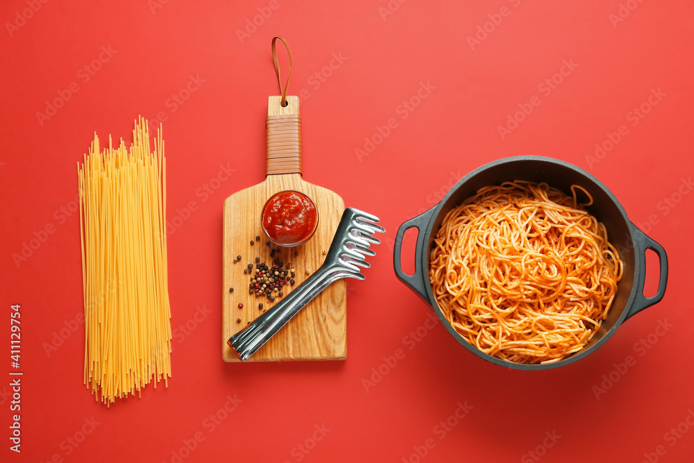 Cooking pot with pasta and ingredients on color background