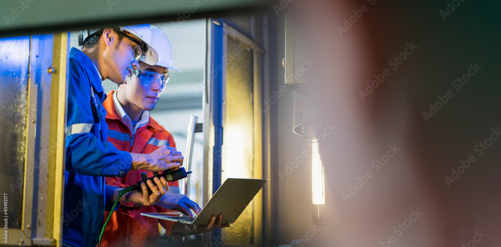 Male Asian engineer professional  having a discussion standing concult cnc machine in the factory ,t