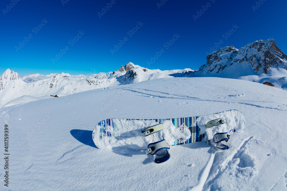 Snowboard lay in the snow on top of the mountains over blue sky on sunny day on ski resort