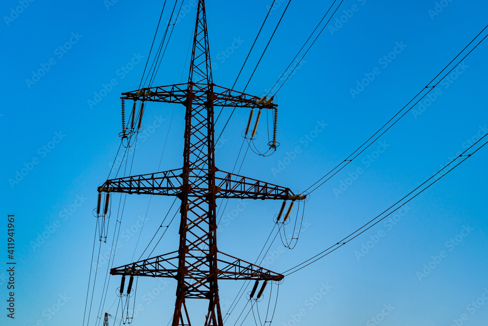 Power poles of a high voltage lines bearing electricity across towns and villages. Selective focus.