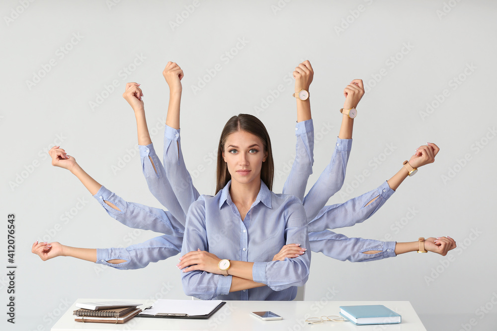 Young woman with a lot of work to do sitting at table on light background