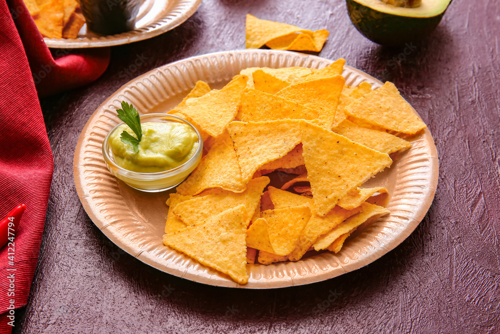 Plate with tasty nachos and sauce on dark background