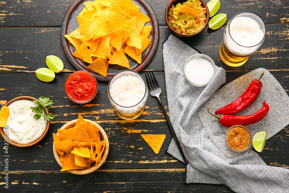 Plates with tasty nachos and sauces on dark wooden background