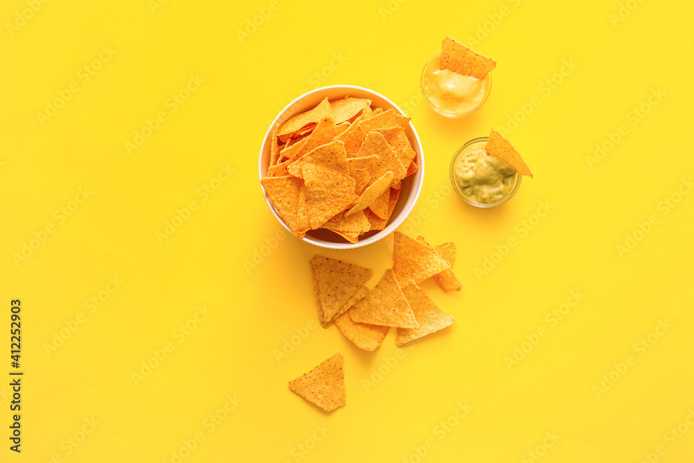 Bowl with tasty nachos and sauces on color background